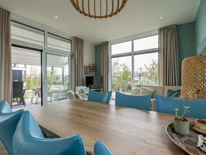 Uma sala de jantar moderna com mesa de madeira, cadeiras azuis e uma janela grande com cortinas.