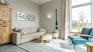 A modern living room with a sofa, coffee table, and a chair. There is a wooden cabinet and a painting on the wall. - Discover this beautiful L-shaped chalet with a covered, sheltered terrace and a lovely lounge set. T (Burgh-Haamstede)