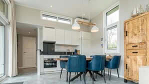 A modern kitchen with white cabinets, a dark countertop, and blue chairs. There is a wooden cabinet with decorative items on top. - Discover this beautiful L-shaped chalet with a covered, sheltered terrace and a lovely lounge set. T (Burgh-Haamstede)