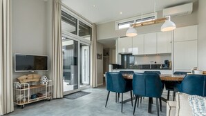 A modern kitchen with white cabinets, a dining area with blue chairs, and a TV on the left. - Discover this beautiful L-shaped chalet with a covered, sheltered terrace and a lovely lounge set. T (Burgh-Haamstede)