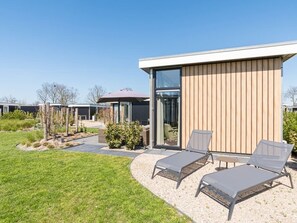 A modern building with a wooden exterior and large glass windows. There are two lounge chairs and a table in the foreground. - With 3 bedrooms and 2 bathrooms, this chalet is one of the most spacious in its category. Inside you (Burgh-Haamstede)