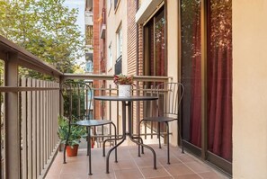 Ein Balkon mit zwei Tischen, Stühlen, einem Blumentopf und Blick auf Gebäude.