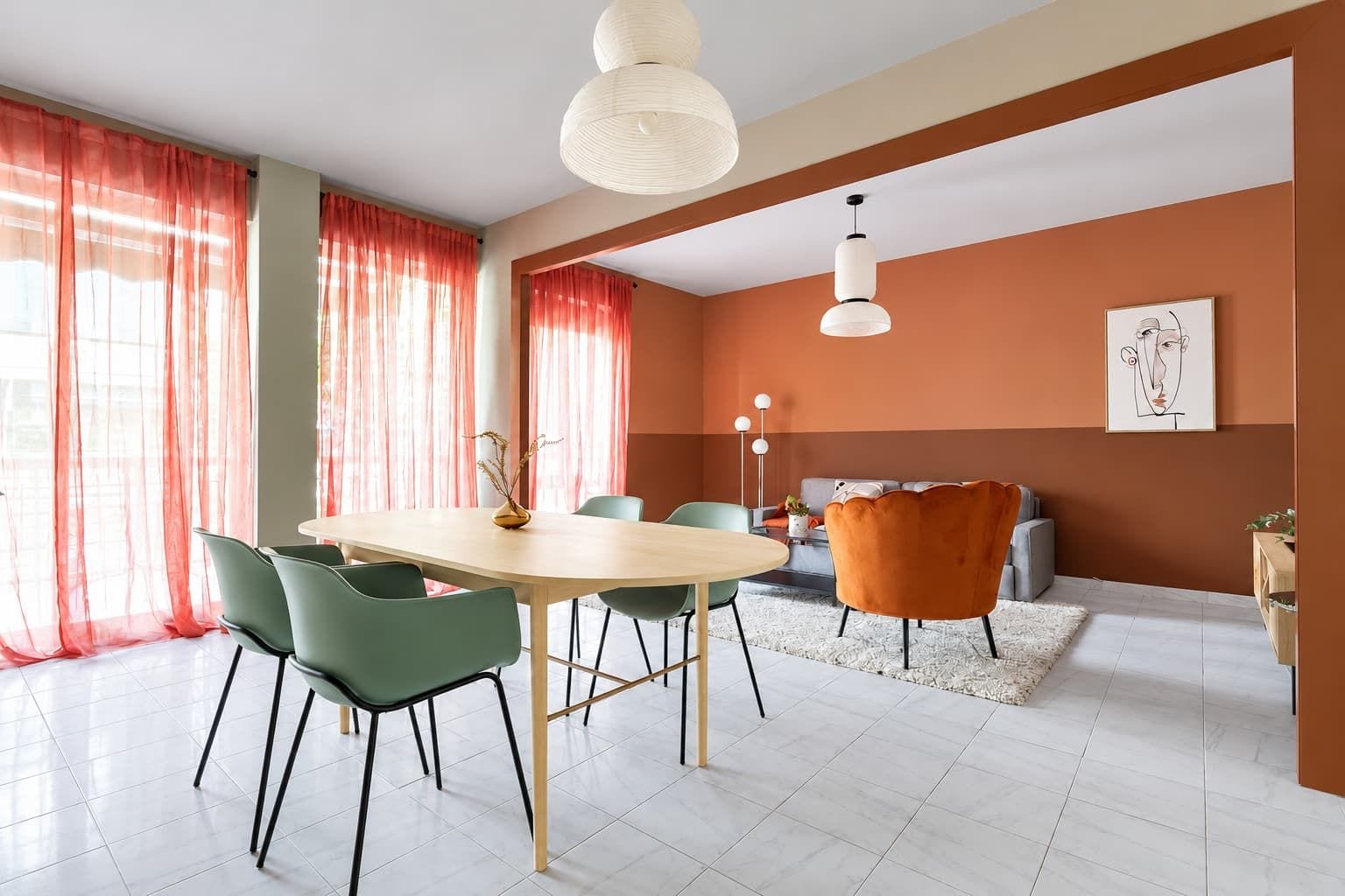 A modern living room with a dining area, featuring a light-colored table, green chairs, a sofa, and a decorative vase.