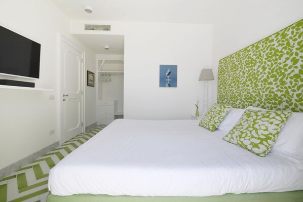 Een slaapkamer met een groot bed, een aan de muur bevestigde televisie en een hoofdeinde met een groen patroon.