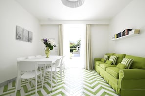 Een moderne woonkamer met een groene bank, een witte eettafel met stoelen, en een groen-witte visgraatvloer.