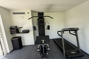 Un petit ensemble d’entraînement à domicile comprenant un tapis de course, un banc de musculation et un appareil d’exercice fixé au mur.