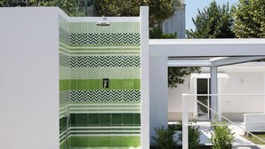 Een moderne buitendouche met groene en witte betegelde vloer, een metalen douchekop en een witte bank.