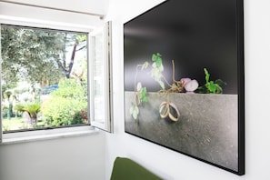Een kamer met een groot raam en een wanddecoratie waarop een plant met vruchten staat afgebeeld.