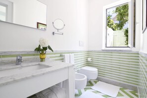 Een badkamer met een wit wastafelmeubel, een spiegel, een toilet en een raam met uitzicht op groen.