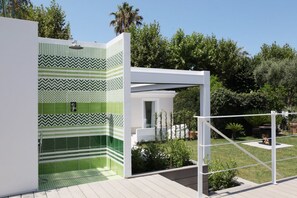 Une salle de bain extérieure moderne, avec des carreaux à motifs verts et une structure blanche.