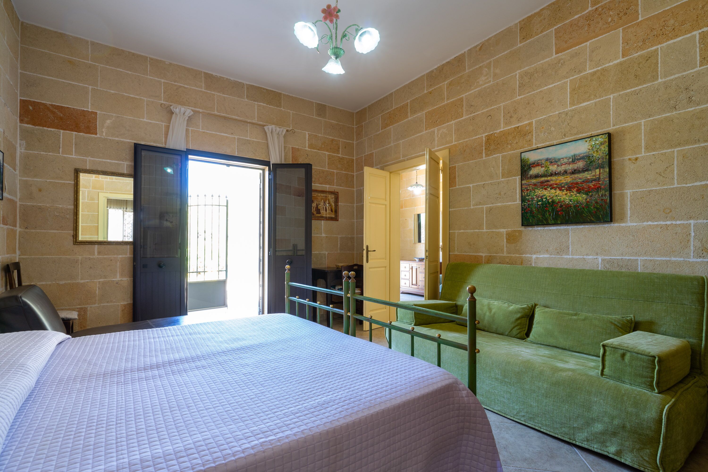 A room with a bed, a green sofa, a painting, and a door leading to another room.