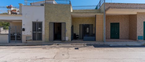 Un edificio de dos pisos con balcón, entrada protegida por un portón y puerta visible.