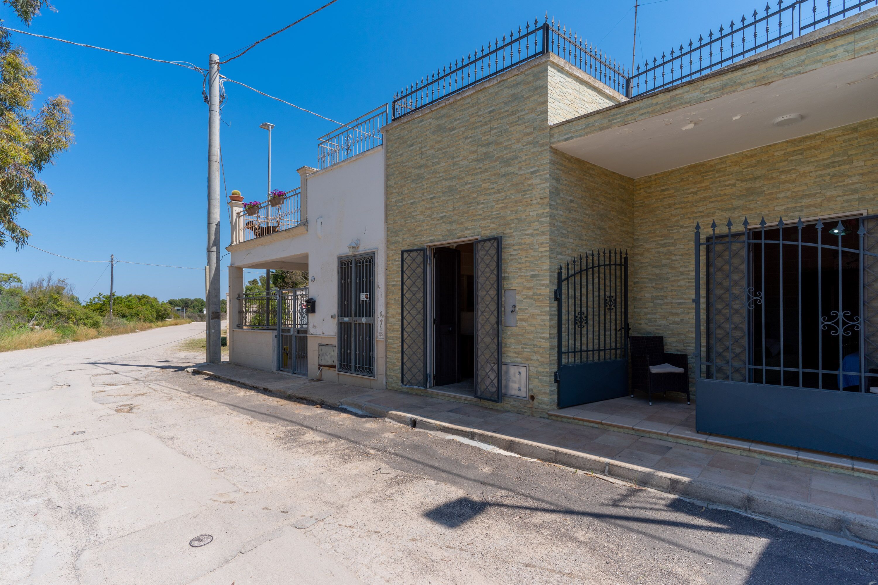 Un edificio de dos pisos con balcón en el nivel superior, entrada protegida por un portón y un pequeño espacio al aire libre para sentarse.
