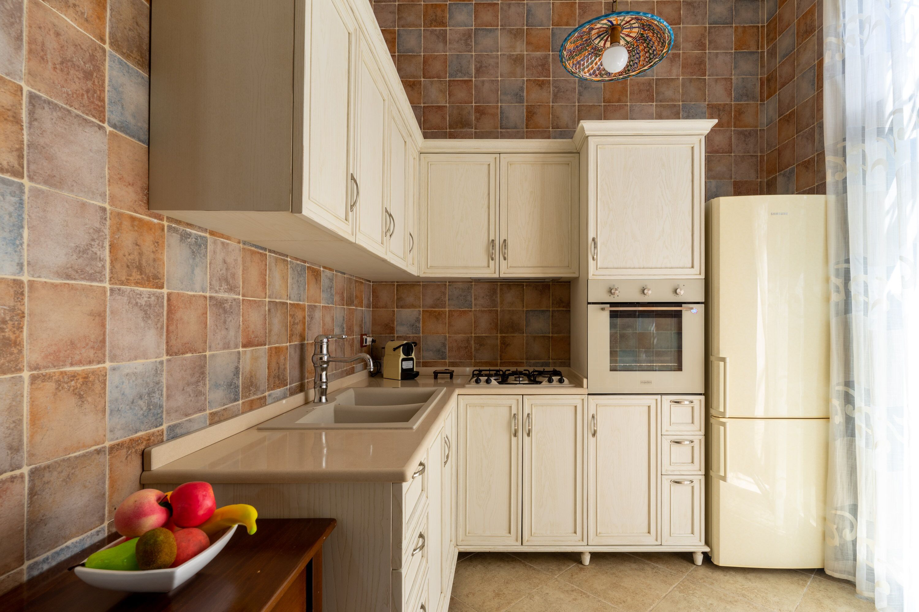 Une cuisine avec des armoires de couleur beige, un évier, une cuisinière et un réfrigérateur.