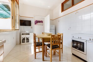 A kitchen with white tiles, a wooden dining table with chairs, a TV mounted above the counter, and a refrigerator. - 3455 Casa Miranda by Barbarhouse (Porto Cesareo)