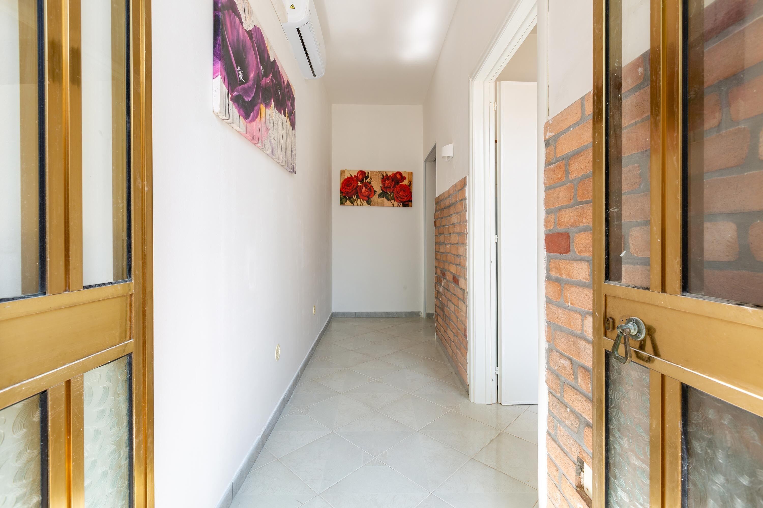 Un couloir avec un sol carrelé, une porte dotée d’un panneau de verre et un mur en briques.
