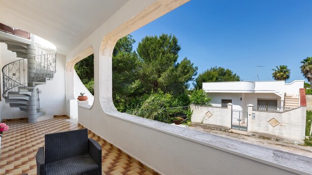 Ein modernes Interieur mit einer Wendeltreppe, Korbmöbeln und Blick auf eine Wohngegend mit Bäumen und einem weißen Gebäude.