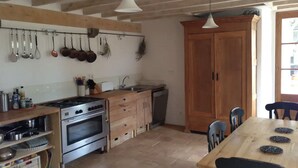 Une cuisine avec des meubles de rangement en bois, une cuisinière et des ustensiles suspendus.