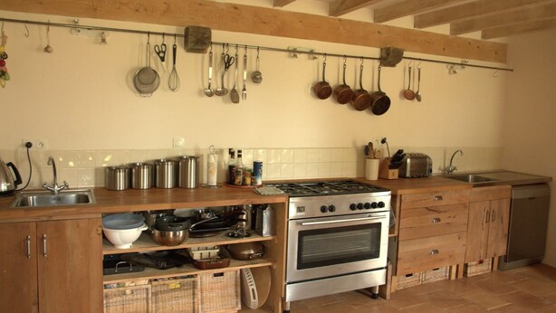 Une cuisine avec des meubles en bois, une cuisinière en acier inoxydable et des casseroles suspendues.