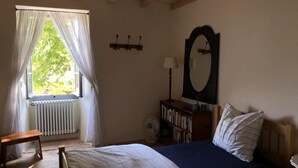 Une chambre à coucher comprenant un lit, une table de chevet, un miroir, un radiateur, une bibliothèque et une fenêtre avec des rideaux.