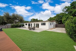Uma casa térrea com um pátio, um pequeno deck e um gramado bem cuidado.