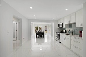 Une cuisine moderne avec des meubles blancs, un coin repas comprenant une table et des chaises, et une vue dégagée par une porte ouverte.