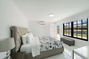 Une chambre à coucher avec un grand lit, une table de chevet, un banc et une fenêtre donnant sur un beau paysage.