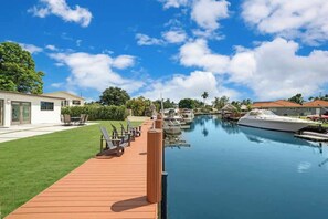 Un port de plaisance avec des bateaux amarrés, une terrasse en bois avec des chaises et un bâtiment moderne doté de grandes fenêtres.