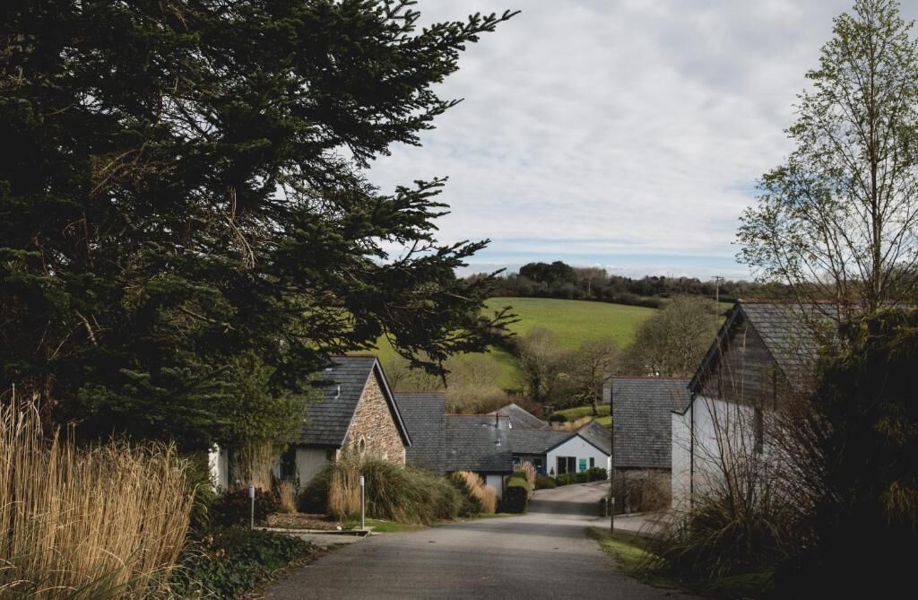 A rural village with stone houses, a narrow road, and a green landscape in the background.