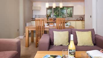 A modern living room with a sofa, a coffee table with magazines and a bottle, and a dining area with chairs and a table.
