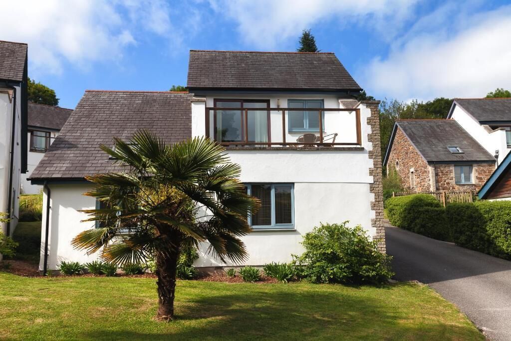A two-story house with a balcony, a well-maintained lawn, and a palm tree.