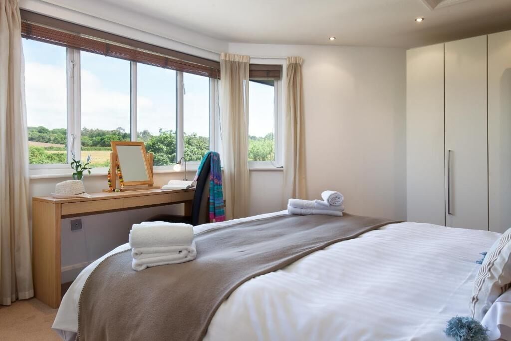 Un dormitorio con una cama grande, un escritorio de madera, un espejo y vistas al exterior.