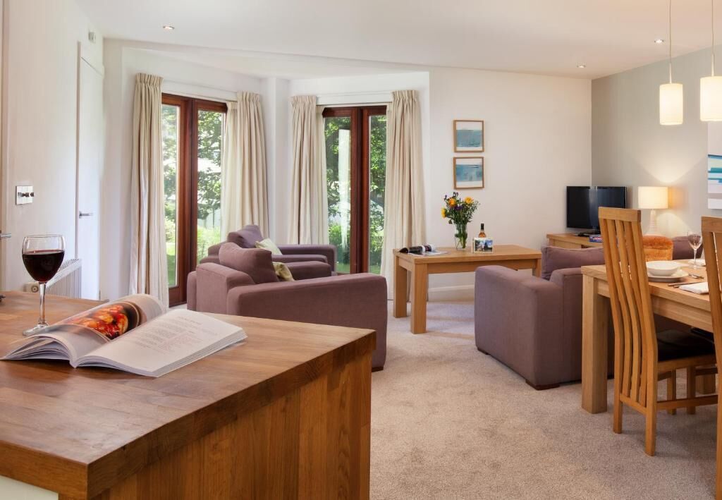 A modern living room with a wooden coffee table, two sofas, a dining table with chairs, and a television.