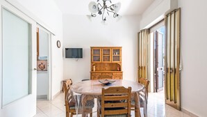 A dining area with a round table, chairs, a wooden cabinet, and a television on the wall. - 3381 Casa Savina by Barbarhouse (Porto Cesareo)