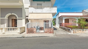 A two-story building with a small shop on the ground floor, featuring a metal gate and a wooden door. - 3381 Casa Savina by Barbarhouse (Porto Cesareo)