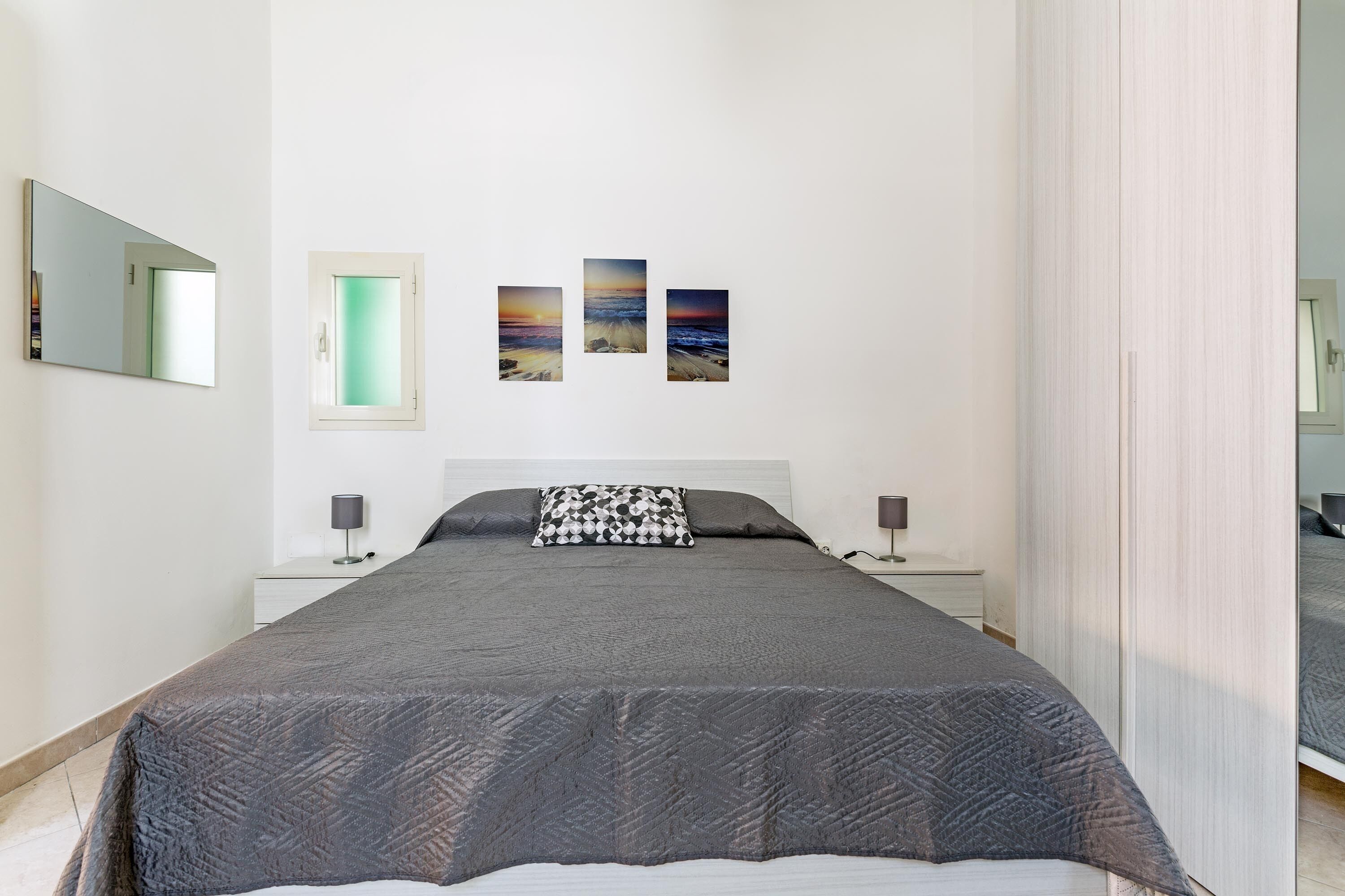 A bedroom with a large bed, two bedside tables, a nightstand, and three wall-mounted pictures depicting landscapes.