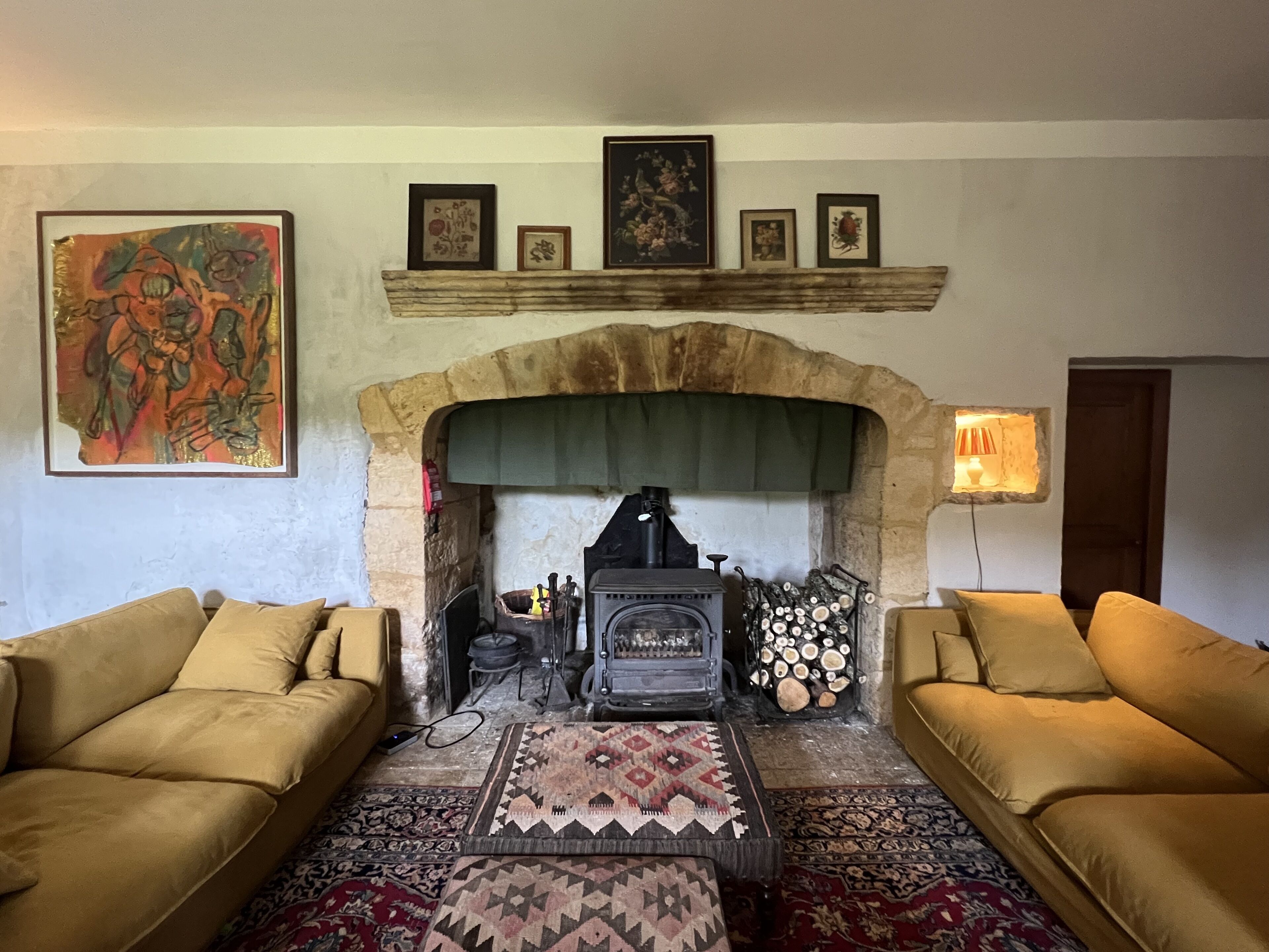 A cozy living room with a stone fireplace, two sofas, a patterned rug, and framed artwork on the wall.