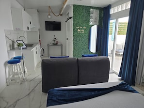 A modern room with a bed, a small kitchenette, a dining area, and a view of the outdoors.