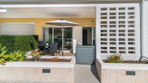 Een terras met een tafel, stoelen, een witte parasol en een pergola met planten.
