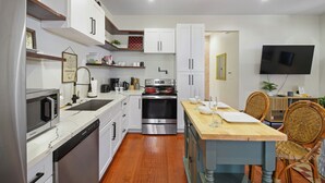 Una cocina moderna con muebles blancos, horno empotrado y una mesa de comedor de madera con sillas.