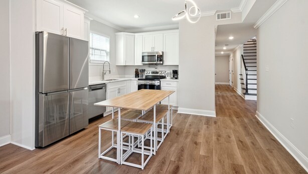 Una cocina moderna con armarios blancos, electrodomésticos de acero inoxidable y una mesa de comedor de madera.