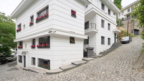 Un immeuble blanc à plusieurs étages, doté de balcons, d’un escalier en pierre et d’une voiture garée.