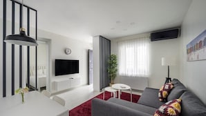 Un salon moderne avec un canapé gris, une table à manger blanche et un tapis rouge.