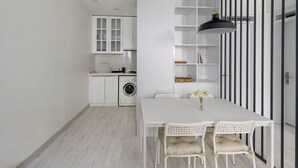 Une cuisine moderne avec des meubles blancs, un lave-linge et un coin repas comprenant une table et des chaises blanches.