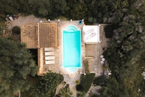 Oversigtsbillede af en ejendom med swimmingpool, overdækket terrasse og en lille have.