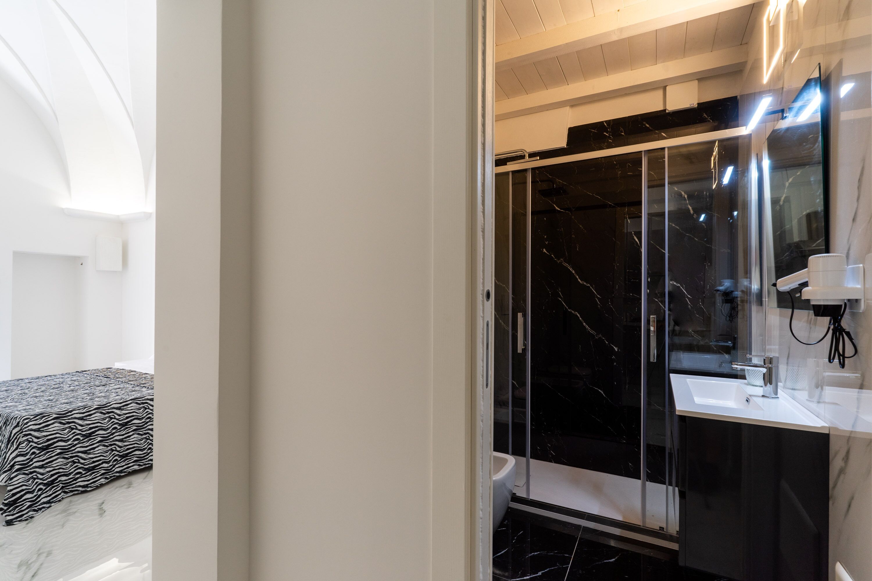 Un baño moderno con ducha envuelta en vidrio, un lavamanos blanco y una cómoda con encimera de mármol.