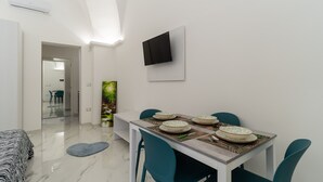 Un comedor moderno con una mesa blanca preparada para cuatro, sillas color turquesa y un televisor de pantalla plana montado en la pared.