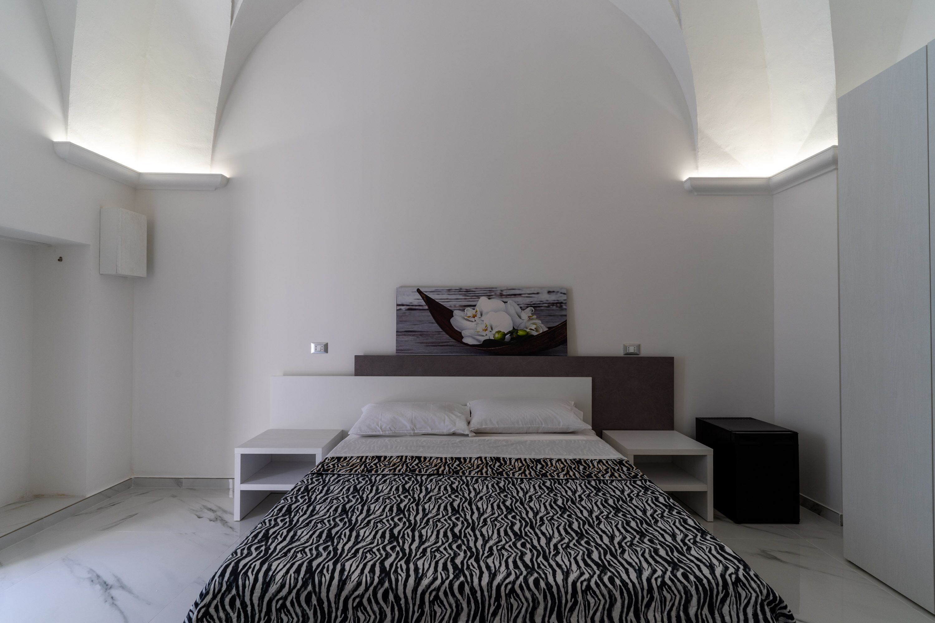 Un dormitorio moderno con una cama, una mesita de noche y una repisa en la pared.