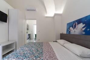 Une chambre à coucher avec un lit, un téléviseur fixé au mur et un tableau représentant des cygnes.