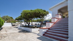 A building with a staircase leading to a white entrance, surrounded by trees and parked cars.